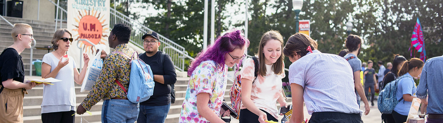 students collect brochures while being assisted by staff at an information table while crowds chat in the background on the Quad in front of the library on the northwest Denver campus