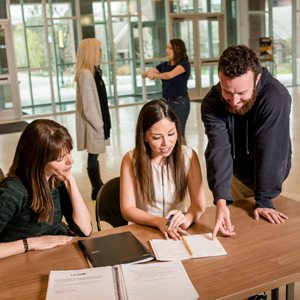 three students collaborate at a table, reviewing notes and documents in a bright, modern study space at Regis University