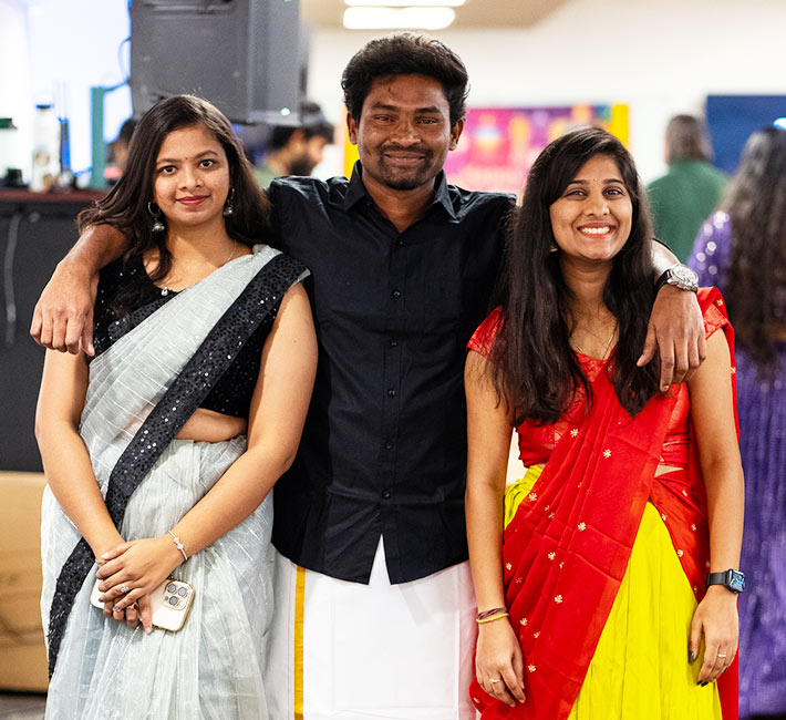 three international students smile and pose while wearing the traditional clothing from their home country