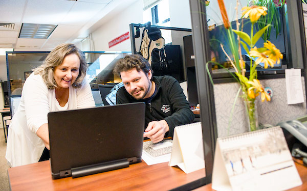 University staff work together on a laptop computer in an office, smiling and enrolling new students in online OCICU courses.