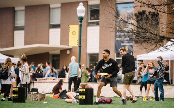 students gather on the grassy Commons playing frisbee and socializing near tents and activity booths