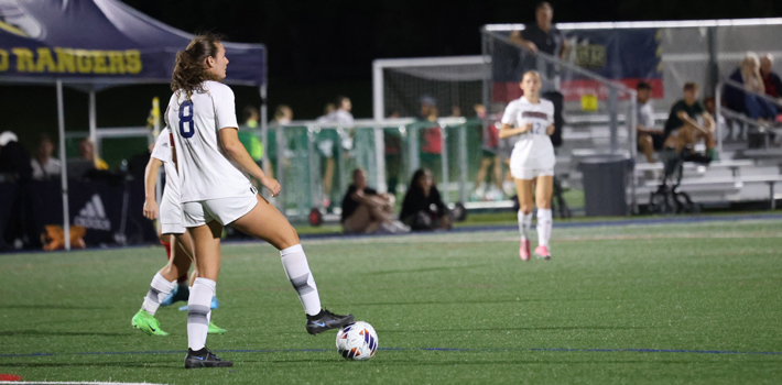 Cullinan wearing jersey number 8 in a white uniform holds the soccer ball under her right foot, assessing the field, with teammates and spectators in the background