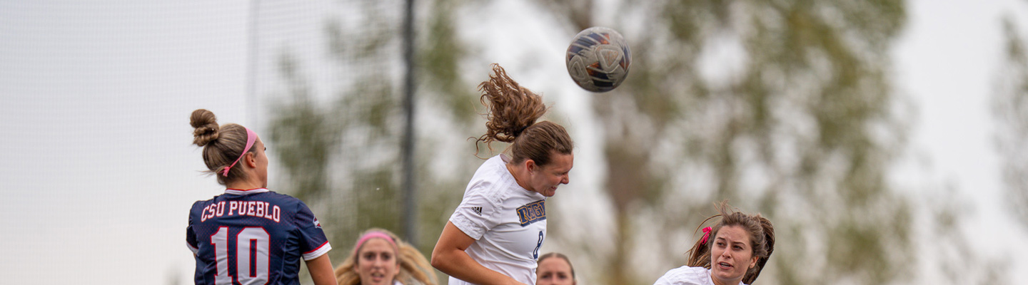 Cullinan heads the soccer ball while opponents and teammates nearby watch