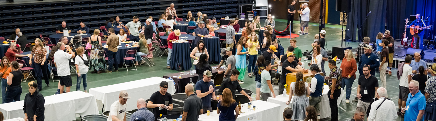 Guests enjoying the 2024 Regis University Blue and Gold Weekend Iggy Beer Festival indoors with food, drinks, live music, and socializing at tables and vendor booths.
