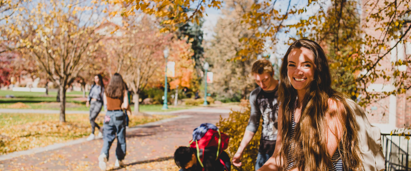 students enjoy autumn on campus, gathering fallen leaves under golden trees