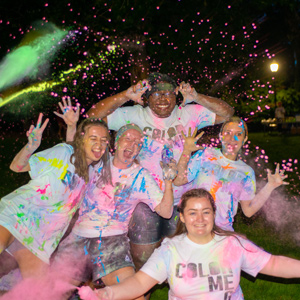 group of alumni holding hands and making silly faces, wearing Color Run event t-shirts covered in bright paint
