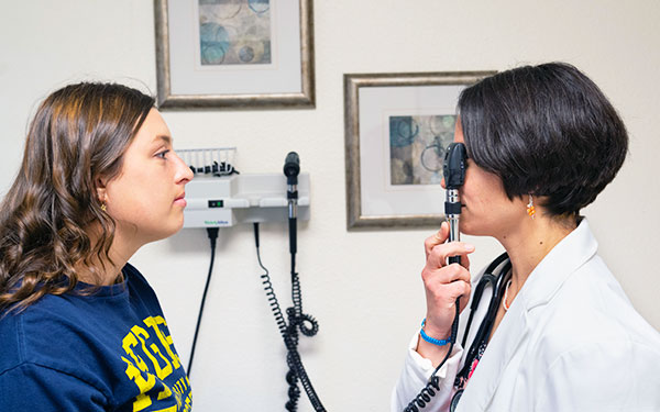 Student on the left looking right and doctor on the right looking left at the student with medical instrument